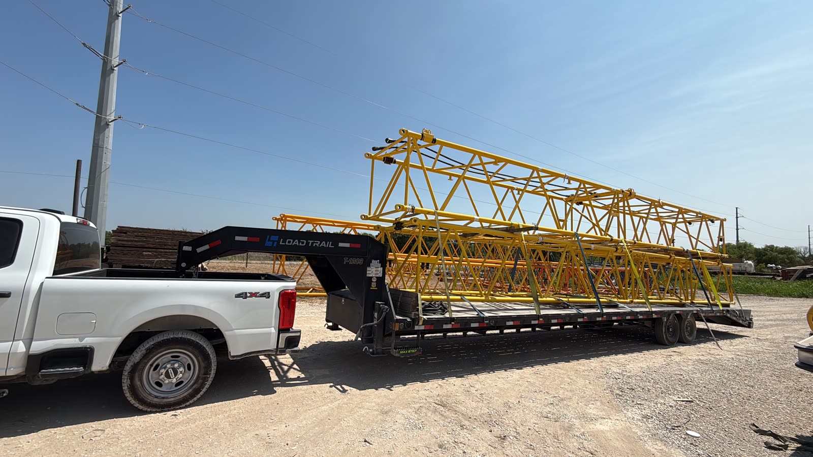 A white heavy-duty pickup pulling a gooseneck trailer loaded with yellow crane boom sections